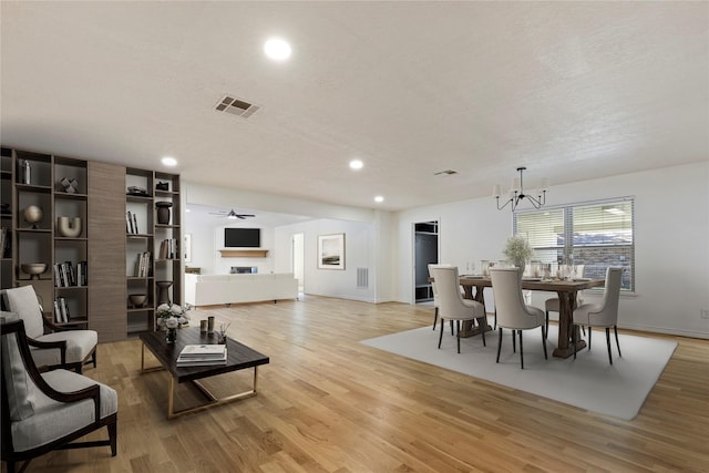 dining area featuring ceiling fan with notable chandelier, light wood-type flooring, and a textured ceiling