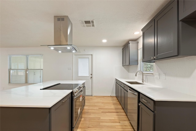 kitchen featuring sink, light hardwood / wood-style flooring, a textured ceiling, island exhaust hood, and stainless steel appliances