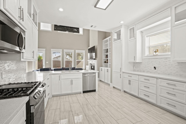 kitchen with sink, kitchen peninsula, decorative backsplash, white cabinetry, and stainless steel appliances