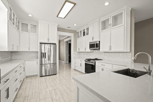 kitchen with sink, stainless steel appliances, tasteful backsplash, light stone counters, and white cabinets