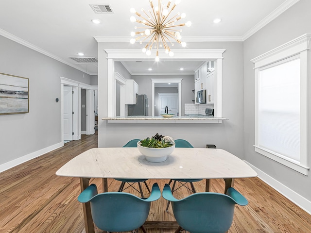 dining space with crown molding, sink, a chandelier, and light hardwood / wood-style floors