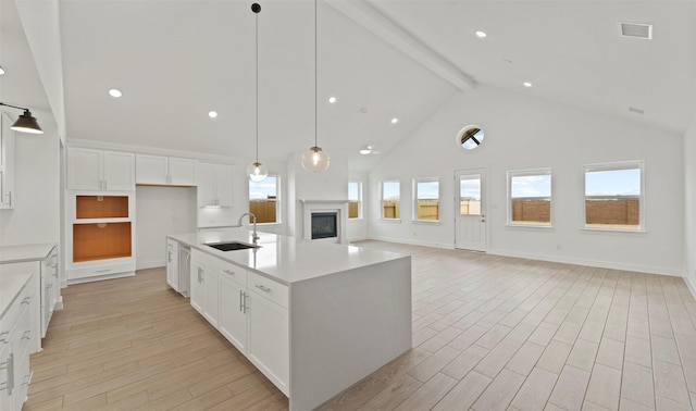 kitchen with beamed ceiling, a center island with sink, white cabinetry, and sink