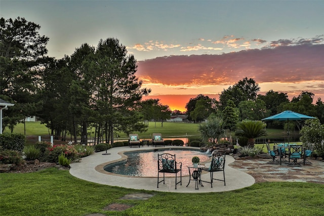 pool at dusk with a patio area and a lawn