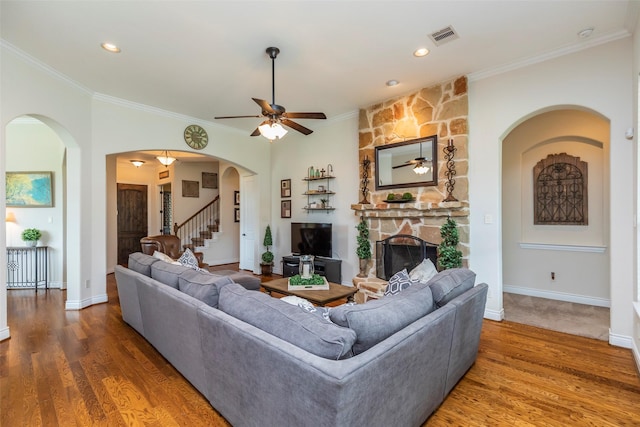 living room with a stone fireplace, hardwood / wood-style floors, ceiling fan, and ornamental molding