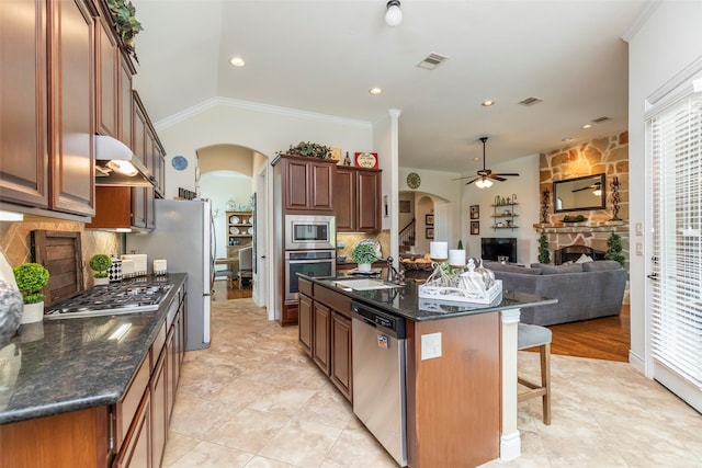 kitchen with a fireplace, a center island with sink, backsplash, and appliances with stainless steel finishes