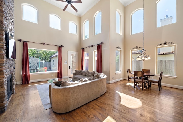 living room featuring ceiling fan with notable chandelier, hardwood / wood-style flooring, a stone fireplace, and ornamental molding