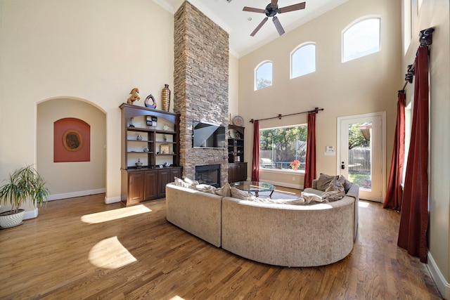 living room featuring ceiling fan, a high ceiling, wood-type flooring, a fireplace, and ornamental molding