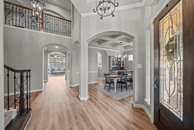 entryway with a towering ceiling, ornamental molding, coffered ceiling, wood-type flooring, and a chandelier