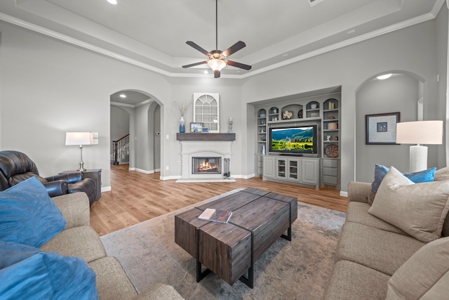 living room featuring a tray ceiling, built in shelves, crown molding, and wood-type flooring