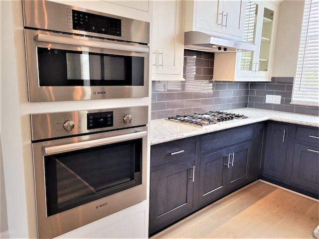 kitchen featuring decorative backsplash, appliances with stainless steel finishes, light hardwood / wood-style floors, light stone counters, and white cabinetry