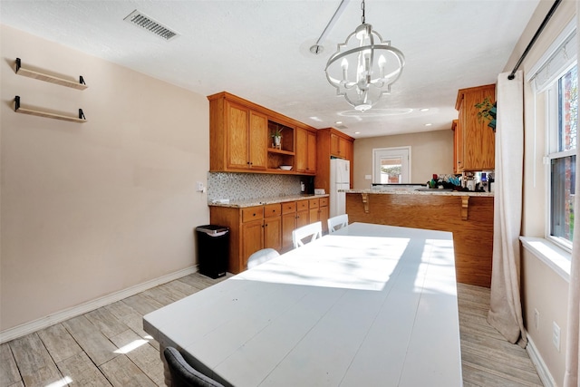 kitchen with pendant lighting, backsplash, white refrigerator, light hardwood / wood-style flooring, and kitchen peninsula