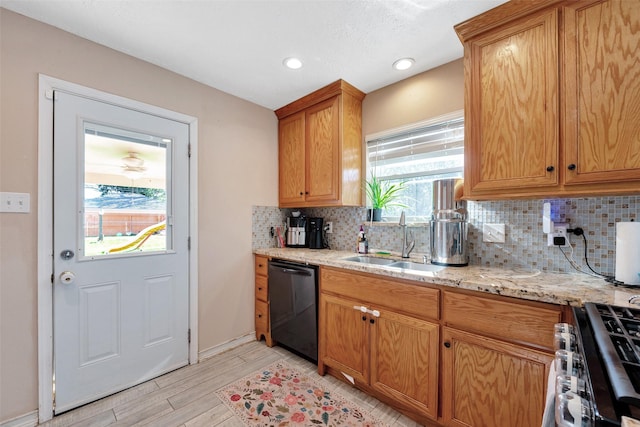 kitchen featuring sink, light wood-type flooring, black dishwasher, light stone counters, and stainless steel range with gas stovetop