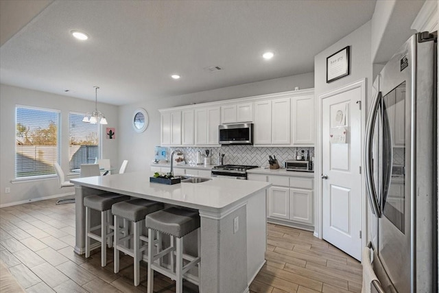 kitchen with stainless steel appliances, sink, decorative light fixtures, white cabinetry, and an island with sink