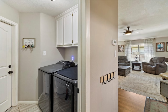 laundry area featuring a textured ceiling, washer and clothes dryer, cabinets, ceiling fan, and light hardwood / wood-style flooring