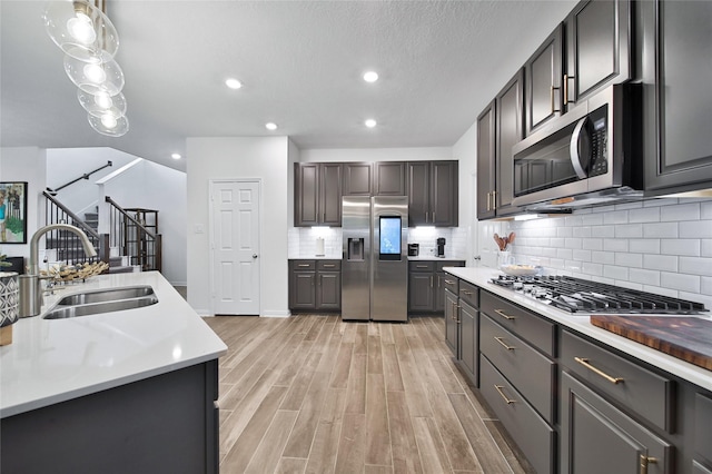 kitchen featuring sink, hanging light fixtures, stainless steel appliances, light hardwood / wood-style floors, and backsplash