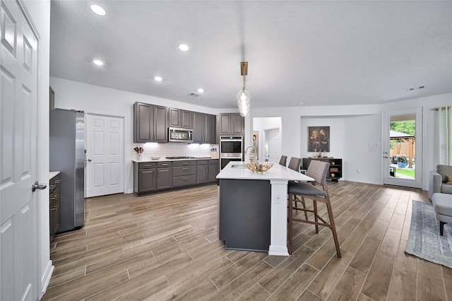 kitchen featuring a breakfast bar area, stainless steel appliances, tasteful backsplash, an island with sink, and light wood-type flooring