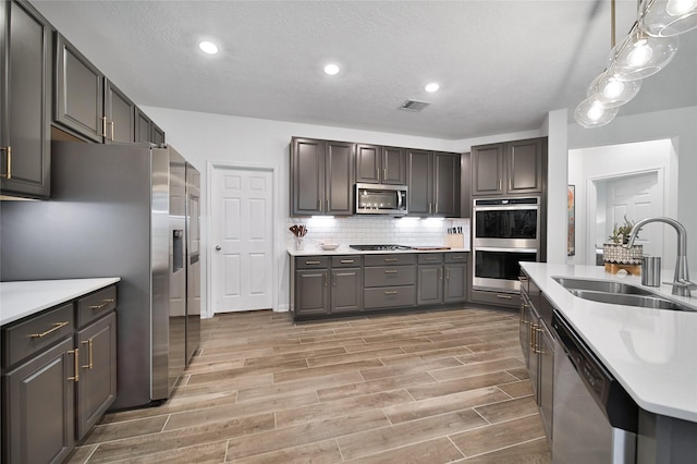 kitchen featuring pendant lighting, sink, appliances with stainless steel finishes, tasteful backsplash, and a textured ceiling