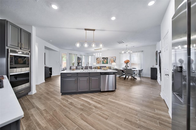 kitchen featuring gray cabinetry, sink, an island with sink, and appliances with stainless steel finishes