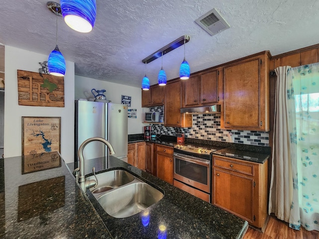 kitchen featuring a textured ceiling, stainless steel appliances, hanging light fixtures, and sink