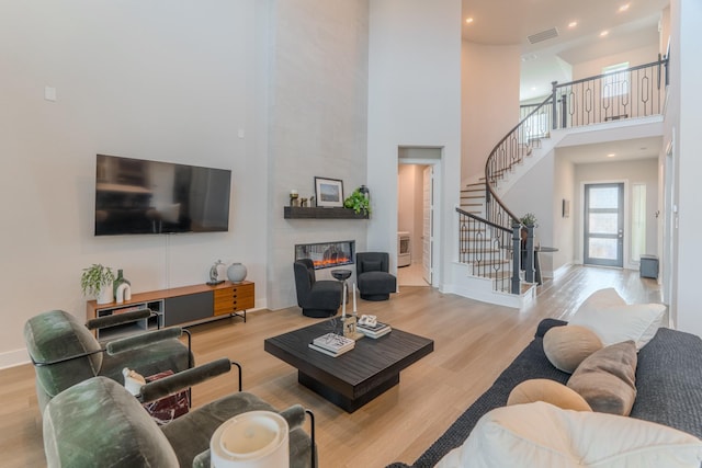 living room with a tile fireplace, light wood-type flooring, and a towering ceiling