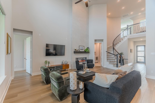 living room with ceiling fan, a fireplace, a high ceiling, and light hardwood / wood-style flooring