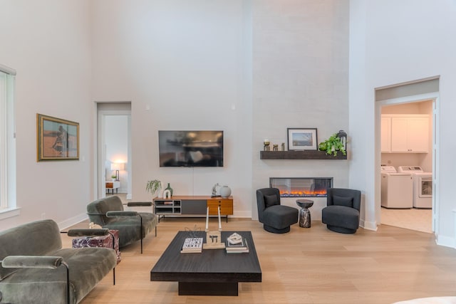 living room with light wood-type flooring, a towering ceiling, separate washer and dryer, and a large fireplace