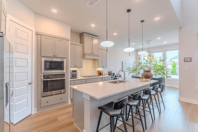 kitchen with pendant lighting, a kitchen island with sink, sink, gray cabinets, and stainless steel appliances