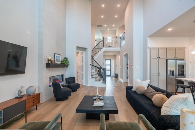 living room with light wood-type flooring, a towering ceiling, and a tiled fireplace