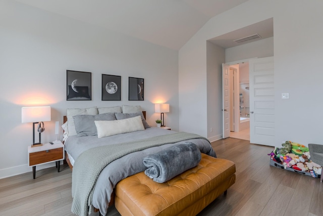 bedroom with wood-type flooring, connected bathroom, and lofted ceiling