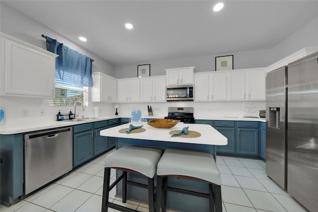 kitchen with blue cabinetry, white cabinetry, a breakfast bar, a kitchen island, and appliances with stainless steel finishes