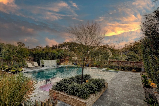 pool at dusk featuring a patio and pool water feature