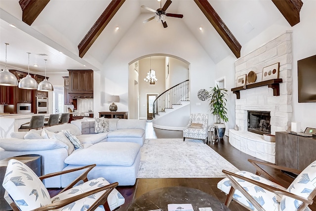 living room with dark hardwood / wood-style flooring, ceiling fan with notable chandelier, high vaulted ceiling, beamed ceiling, and a fireplace