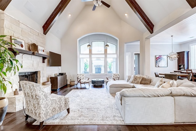 living room with dark hardwood / wood-style flooring, ceiling fan with notable chandelier, high vaulted ceiling, beamed ceiling, and a stone fireplace