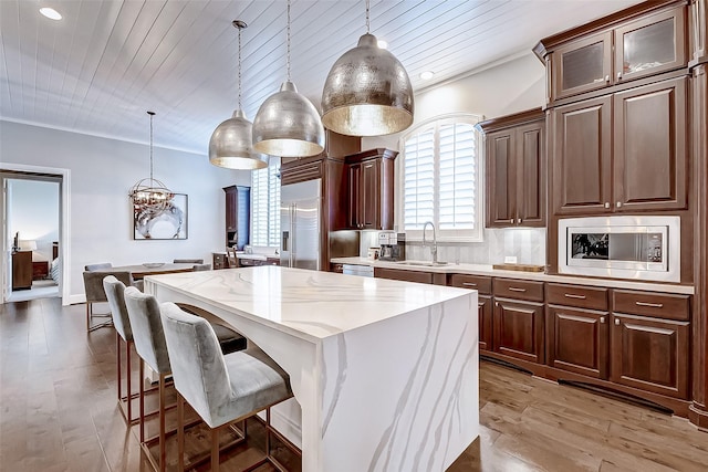 kitchen featuring a center island, built in appliances, hanging light fixtures, and sink