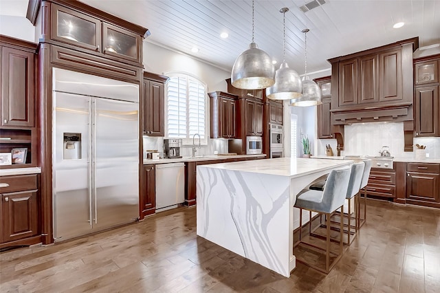 kitchen featuring built in appliances, crown molding, pendant lighting, wood-type flooring, and a kitchen island