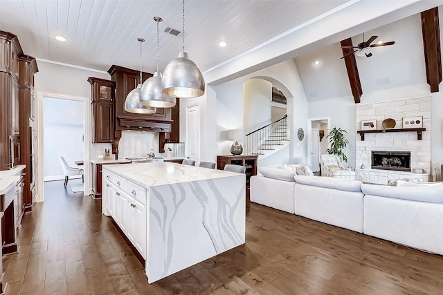 kitchen featuring light stone countertops, dark wood-type flooring, a kitchen island, pendant lighting, and white cabinets