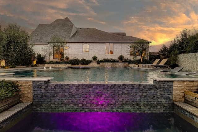 pool at dusk with pool water feature and a patio