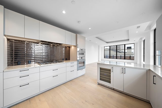 kitchen featuring a raised ceiling, wine cooler, white cabinets, stainless steel appliances, and light wood-type flooring