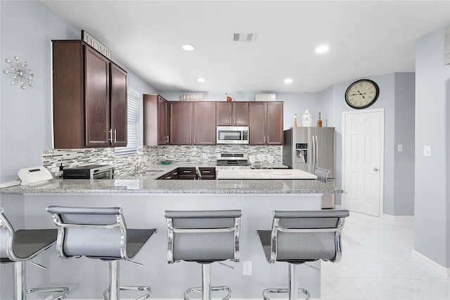 kitchen featuring backsplash, a kitchen bar, kitchen peninsula, and stainless steel appliances