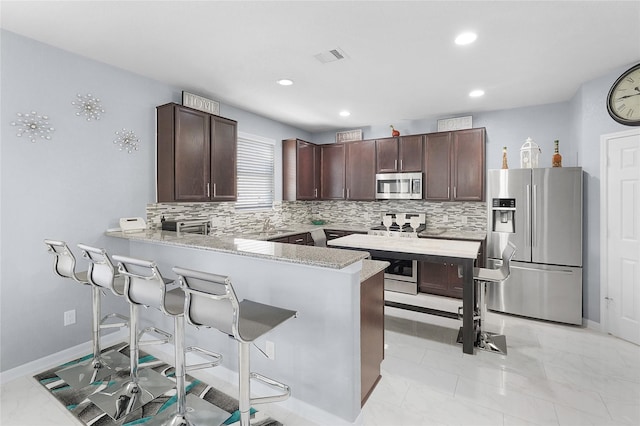 kitchen with a kitchen breakfast bar, kitchen peninsula, dark brown cabinets, and appliances with stainless steel finishes