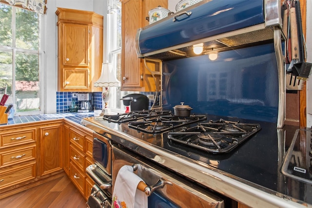 kitchen featuring dark wood-type flooring, gas range, tasteful backsplash, tile counters, and extractor fan