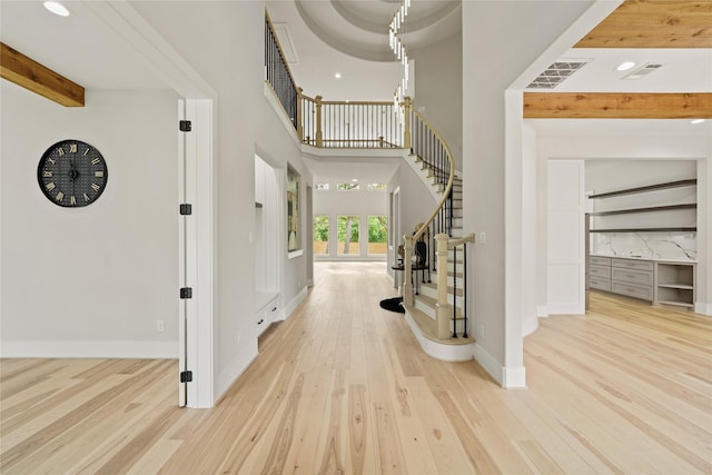 entryway featuring beamed ceiling, light hardwood / wood-style floors, and a high ceiling