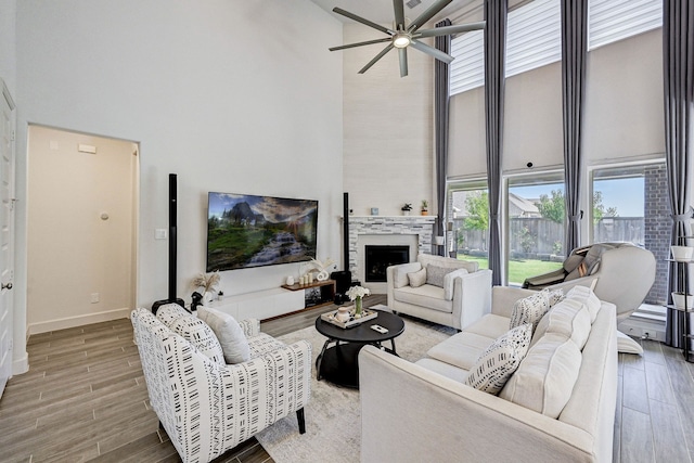 living room featuring a fireplace, a towering ceiling, a ceiling fan, wood finished floors, and baseboards