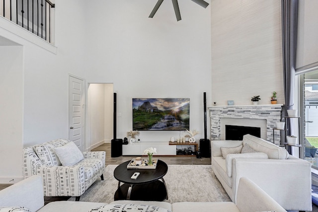 living area with a fireplace, a towering ceiling, light wood-style floors, a ceiling fan, and baseboards