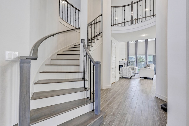 stairway with a fireplace, wood finished floors, a towering ceiling, and baseboards