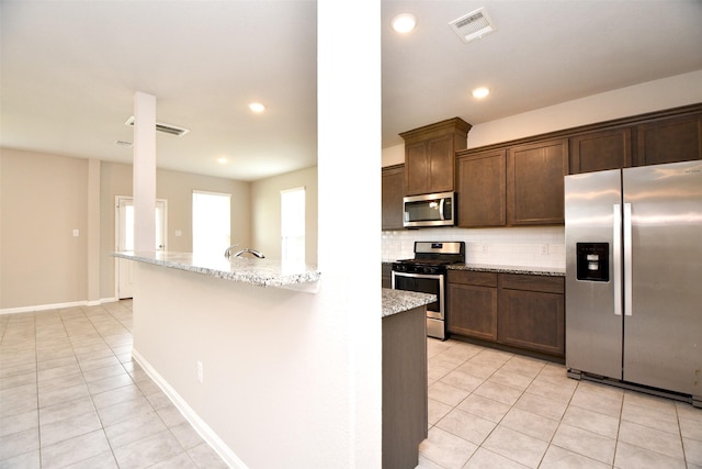 kitchen with decorative backsplash, light stone countertops, stainless steel appliances, and light tile patterned floors