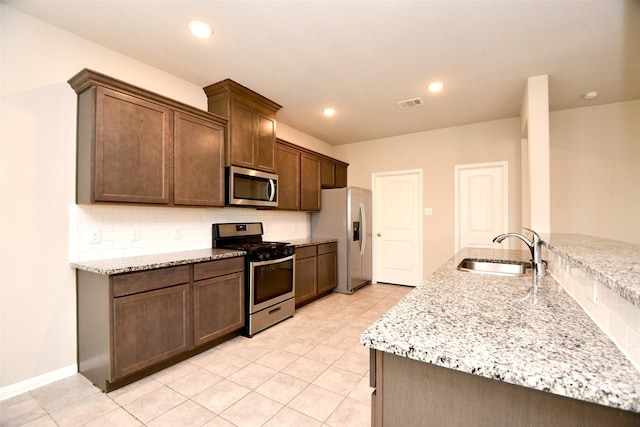 kitchen with sink, light stone countertops, light tile patterned floors, tasteful backsplash, and stainless steel appliances