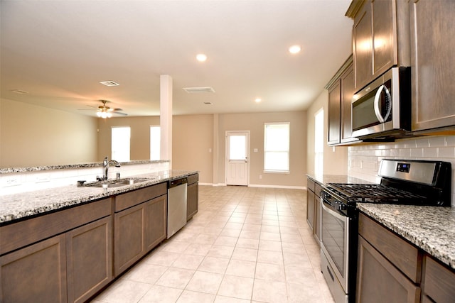 kitchen with sink, ceiling fan, light stone countertops, light tile patterned floors, and stainless steel appliances