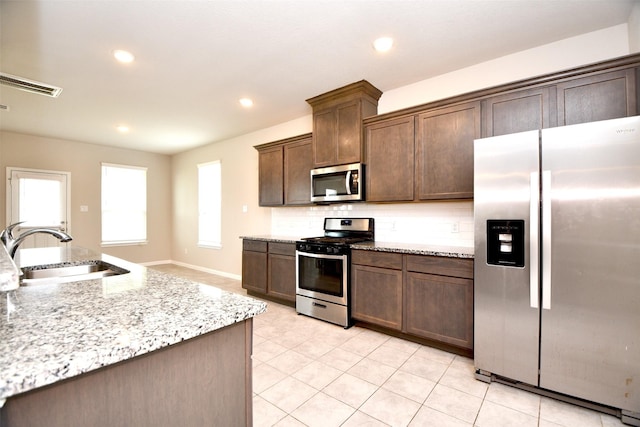 kitchen featuring light stone countertops, sink, stainless steel appliances, backsplash, and dark brown cabinets