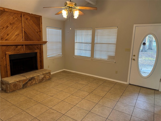 interior space with light tile patterned flooring, ceiling fan, and a stone fireplace